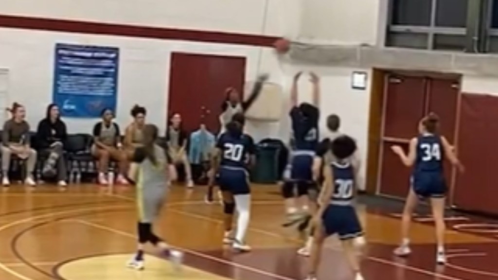 Two women's basketball team players gather near the goal, a one-armed player shoots the ball into the air
