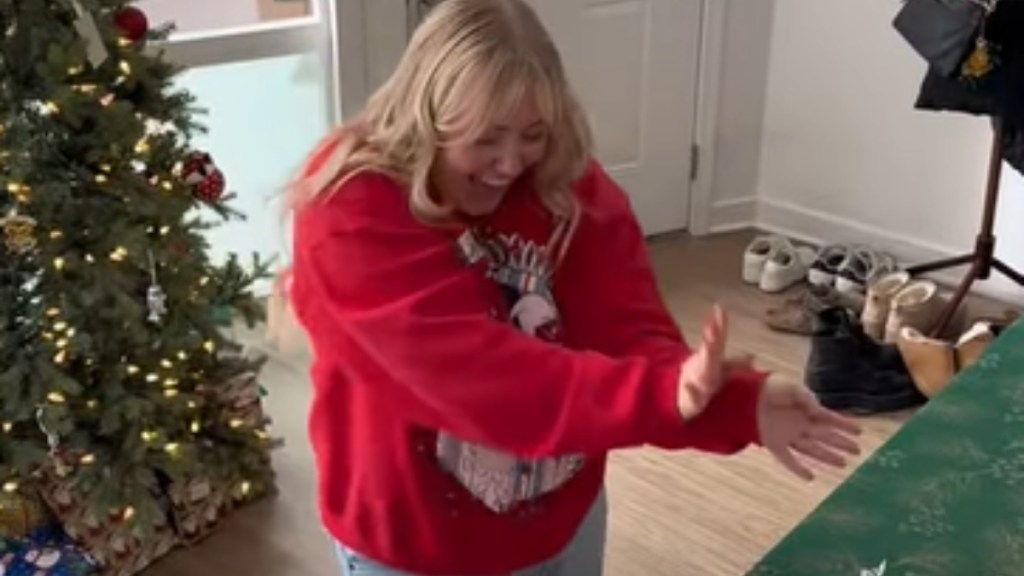 A woman smiles wide, mouth open, as she holds her arms out. She seems to be doing a bit of a happy dance