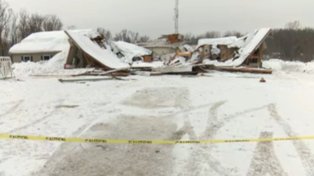 View of a collapsed fire station from behind yellow tape placed to keep people out. Snow is covering the ground and the collapsed building