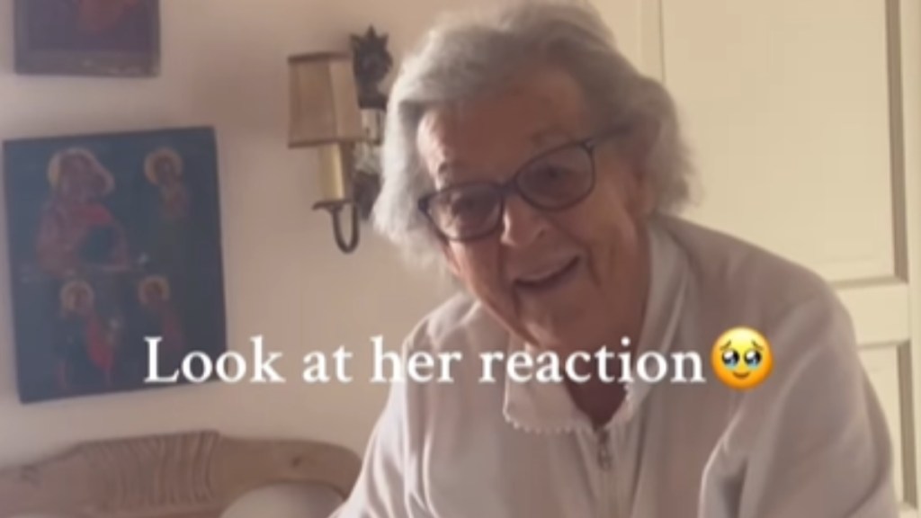 Close up of an elderly woman smiling wide, mouth parted slightly, as she looks over the person capturing this moment. Text on the image reads: Look at her reaction