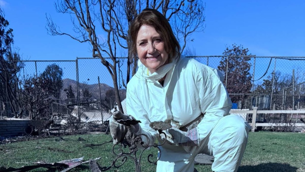 A woman smiles as she kneels on the ground. We can't see what she's posing with but can partially see a burnt lawn decoration