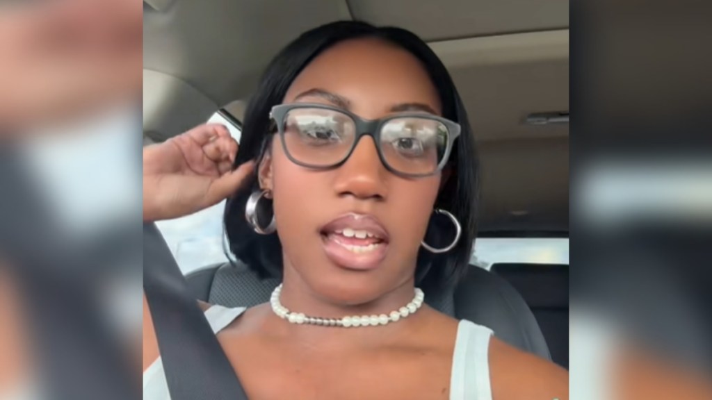 A woman talks into the camera as she sits in her car