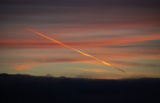 Image shows a contrail creating a golden shadow across the sky at twilight.