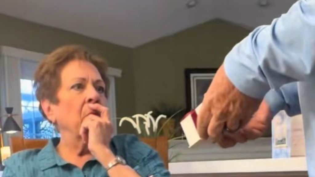 Image shows a man holding out a small box for his wife.