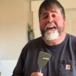 Image shows a husband using a spatula for a microphone as he sings to his wife while making breakfast.