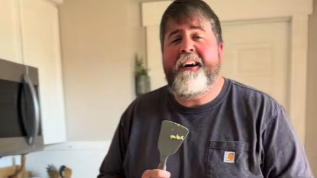 Image shows a husband using a spatula for a microphone as he sings to his wife while making breakfast.