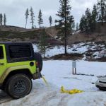 Image shows a Jeep pulling a sedan out of a snowy creek.