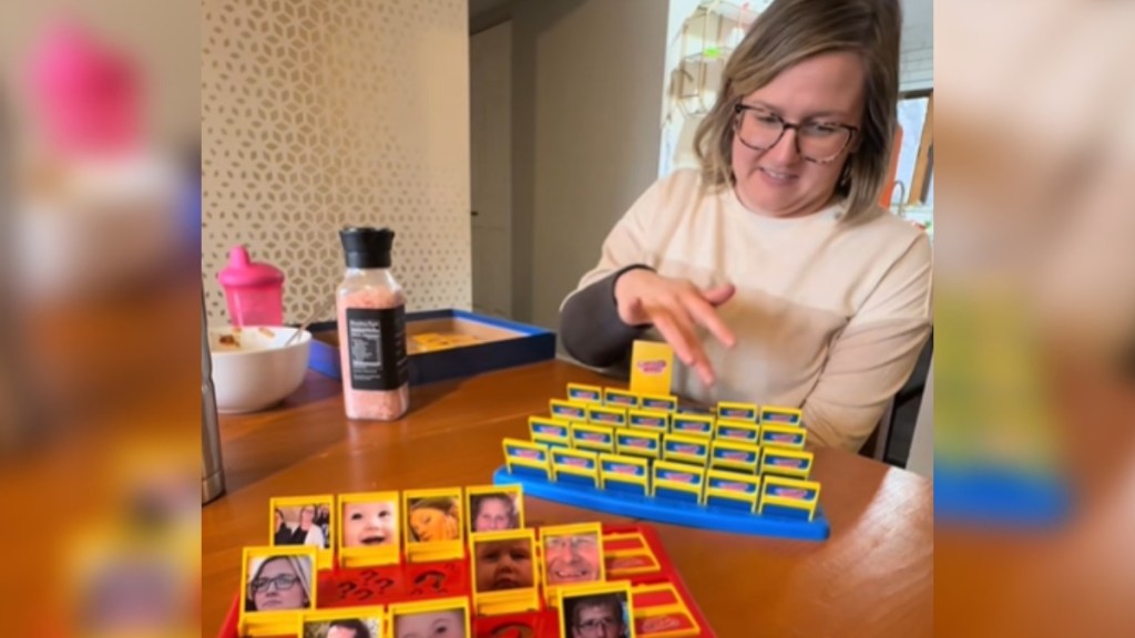 View from someone playing a custom Guess Who game at a dining table. The images are of family. The second player, a woman, concentrates as she closes some of the options on her board