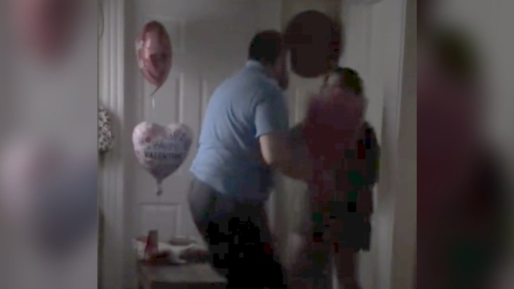 In a darkened room, a man starts to embrace his daughter in a hug. Valentine's balloons are nearby, and it seems there's a bouquet in Dad's hand.