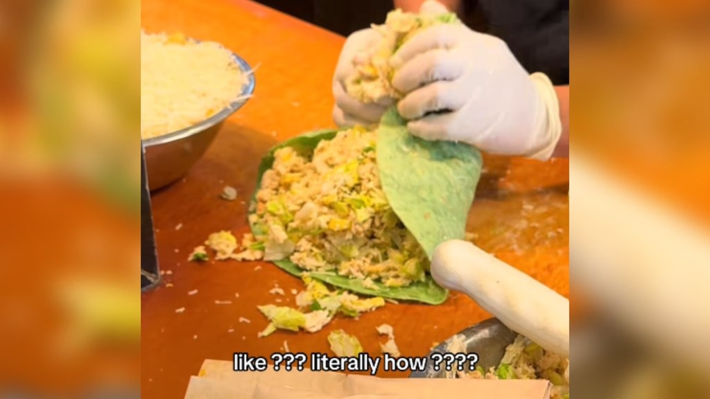 Close up of someone starting to wrap up a giant burrito full of Caesar salad.