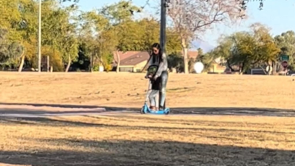 At a distance in a park, a mom and her kid ride on a scooter together