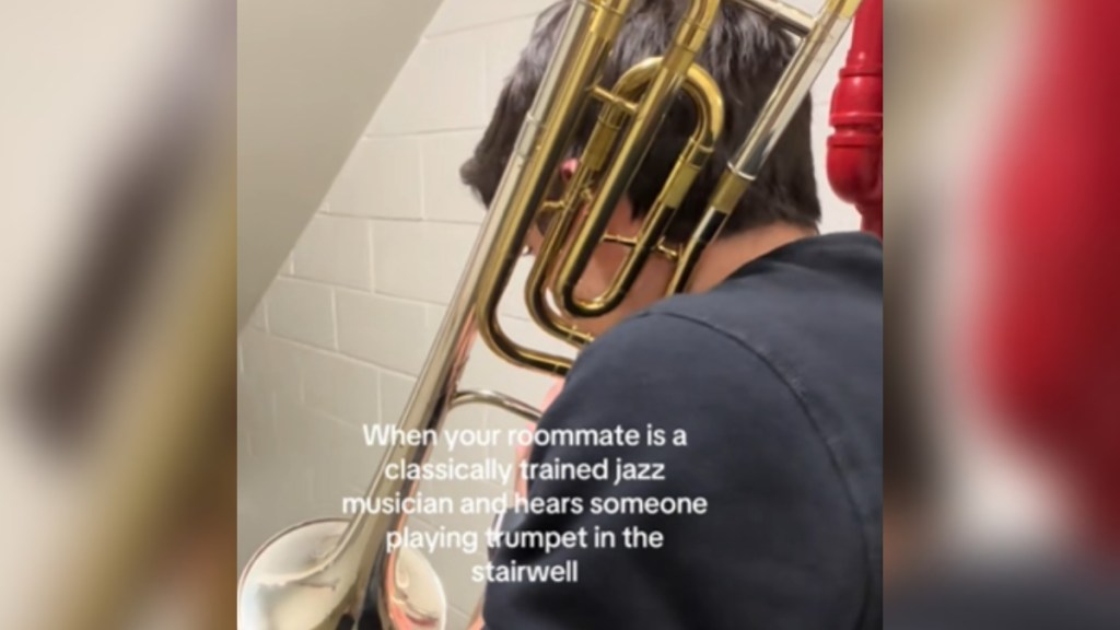 Side-view of a man standing in a stairwell. He looks down as he plays a trumpet. Text on the image reads: When your roommate is a classically trained jazz musician and hears someone playing trumpet in the stairwell