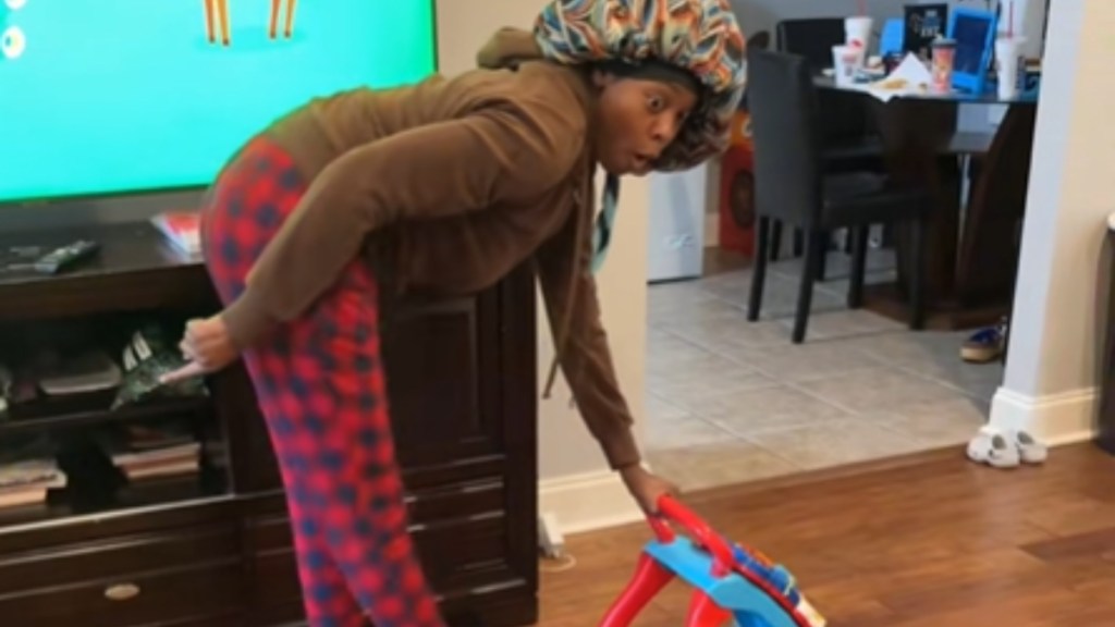 A woman bends over, holding onto a baby walker. She makes a silly face, eyes, wide, as she looks over at the baby who can't be seen in this image.