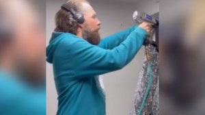 A man wearing headphones uses a power tool on an art piece that can only be partially seen in this image
