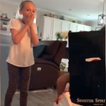 A little girl stands with a shocked expression on her face - her eyes are wide and she covers her mouth with her hands. She's standing near a box. The back of the box is toward the camera. On the back reads: Sinister Spirit