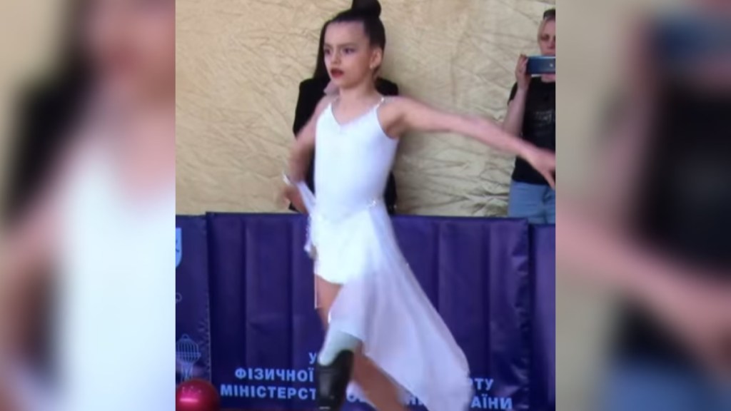 A little girl looks determined as she holds her arms back and moves forward. She has a prosthetic leg and is competing in a dance competition