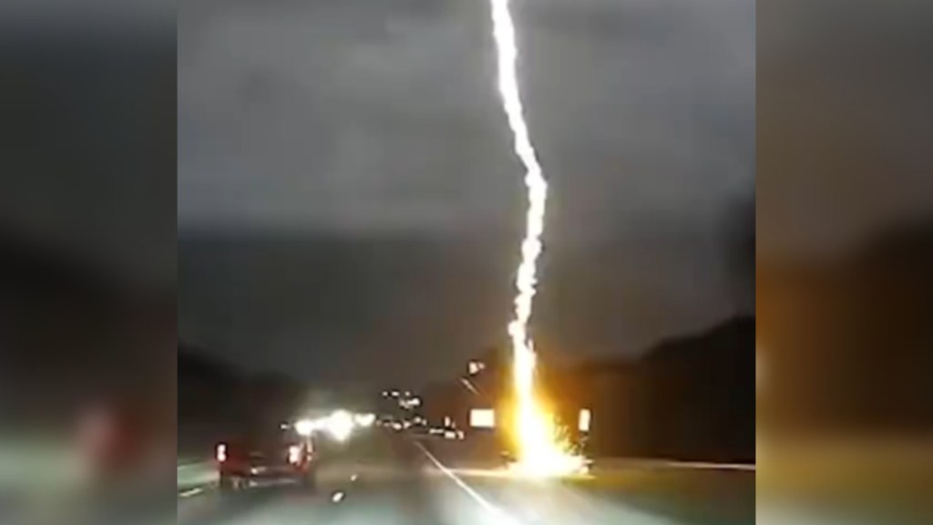 A massive strike of lightning hits a highway, as seen by dashcam footage