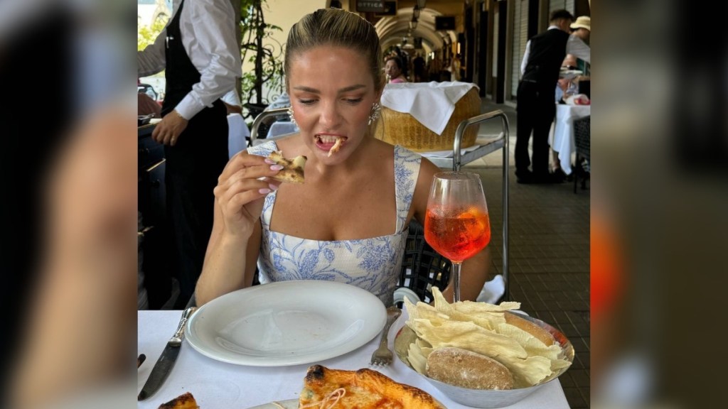 A woman eats a slice of pizza at a restaurant table.