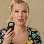 Close up of Millie Bobby Brown holding up a microchip scanner as she talks