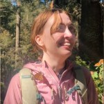 Close up of a smiling woman standing outside during a monarch butterfly migration. She's standing still and looks up in awe. One butterfly rests on top of her head while another sits near her shoulder