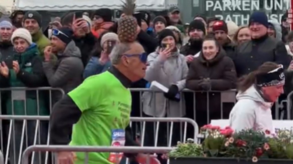 View from the side of a man as he runs in a marathon with a pineapple balanced on his head
