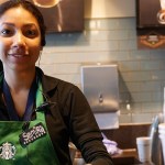 Close up of a Starbucks barista smiling. She's wearing a black button-up shirt and the Starbucks green apron