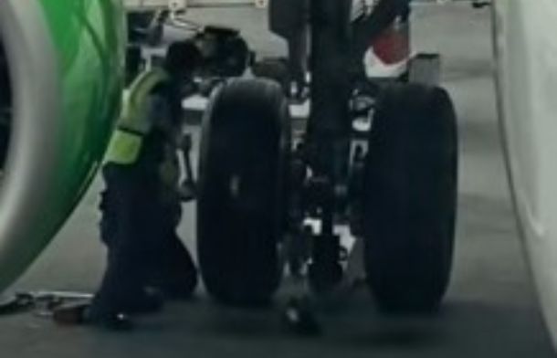 Image shows an aircraft mechanic repairing a flat tire as onlookers share a bit of dad life.