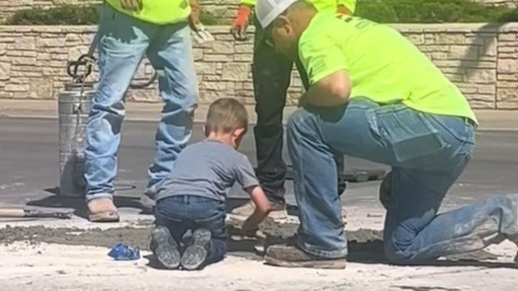 Concrete workers stop to show a young boy how to lay concrete.