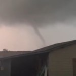 View from a distance of a thin tornado moving behind buildings