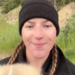 Close up of a smiling woman standing outside. She's starting to lift up something that's fuzzy but it's still unidentifiable.
