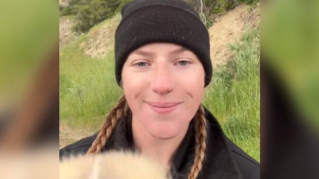 Close up of a smiling woman standing outside. She's starting to lift up something that's fuzzy but it's still unidentifiable.