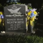 View of a headstone at a grave in the middle of the night. Flowers are on both sides of the headstone.