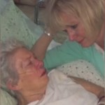 An elderly woman lays in bed. Her adult daughter lays next to her, propped up on her shoulder. The woman looks down at her mom as she speaks