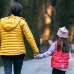 View from behind of a woman and her little girl holding hands as they take a walk outside on a path in nature