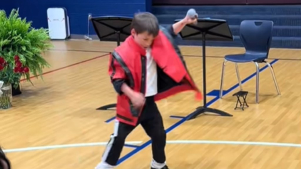 A little boy dressed like Michael Jackson in the "Thriller" music video dances. He holds a mic in his raised hand.