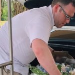 A man picks up a box of flowers from the trunk of a car