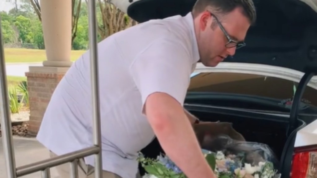 A man picks up a box of flowers from the trunk of a car
